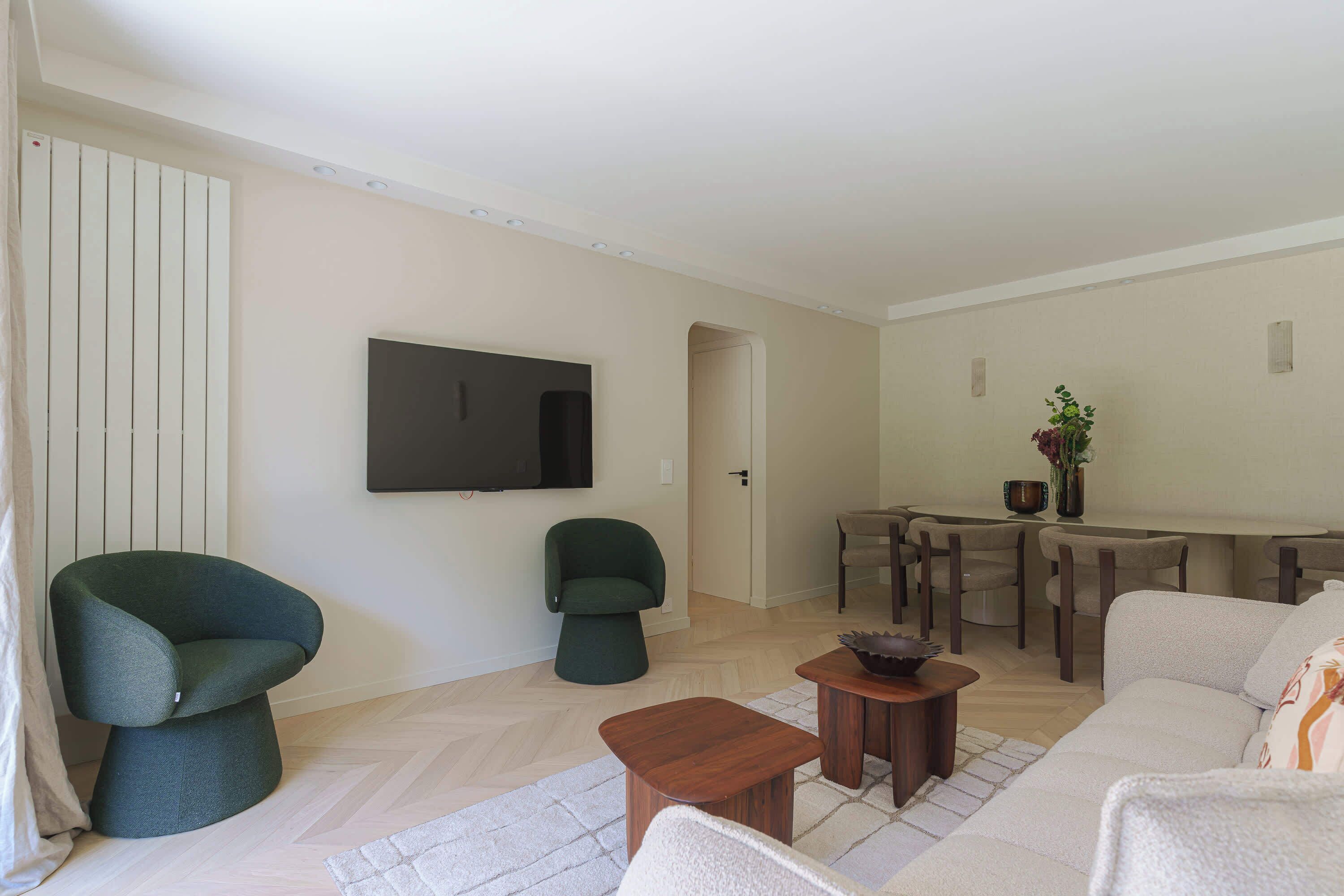Un salon comprenant un canapé, deux fauteuils, une table basse, un téléviseur et un coin repas avec une table et des chaises.