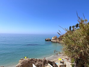 Eine Küstenlandschaft mit Strand, klarem Himmel, felsigem Gelände und Menschen, die das Wasser genießen.