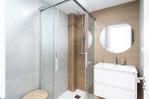 Ein modernes Badezimmer mit einer Duschkabine aus Glas, einem Holzbidet und einem runden Spiegel.