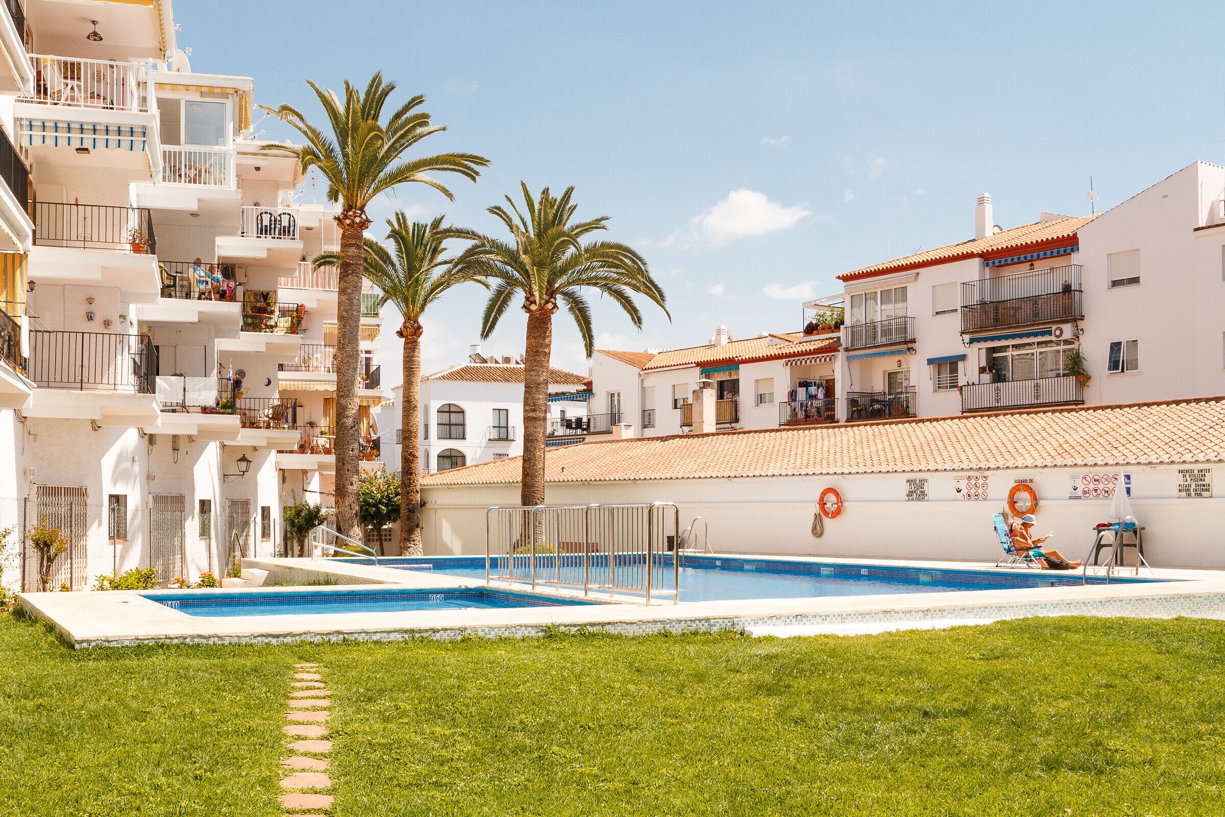 A residential building with a swimming pool, palm trees, and balconies.
