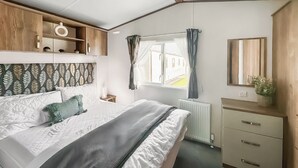 Una camera da letto con un letto, una cassettiera, uno specchio, una finestra con tende e un termosifone.
