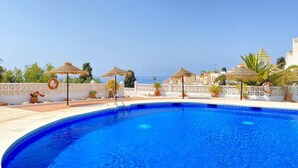 A clear blue pool with a white deck, surrounded by potted plants and thatched umbrellas. - Capistrano Playa 404 by Casasol (Nerja)
