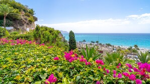 A coastal landscape with vibrant pink flowers, a clear blue sky, and a view of the sea and beach. - Capistrano Playa 404 by Casasol (Nerja)