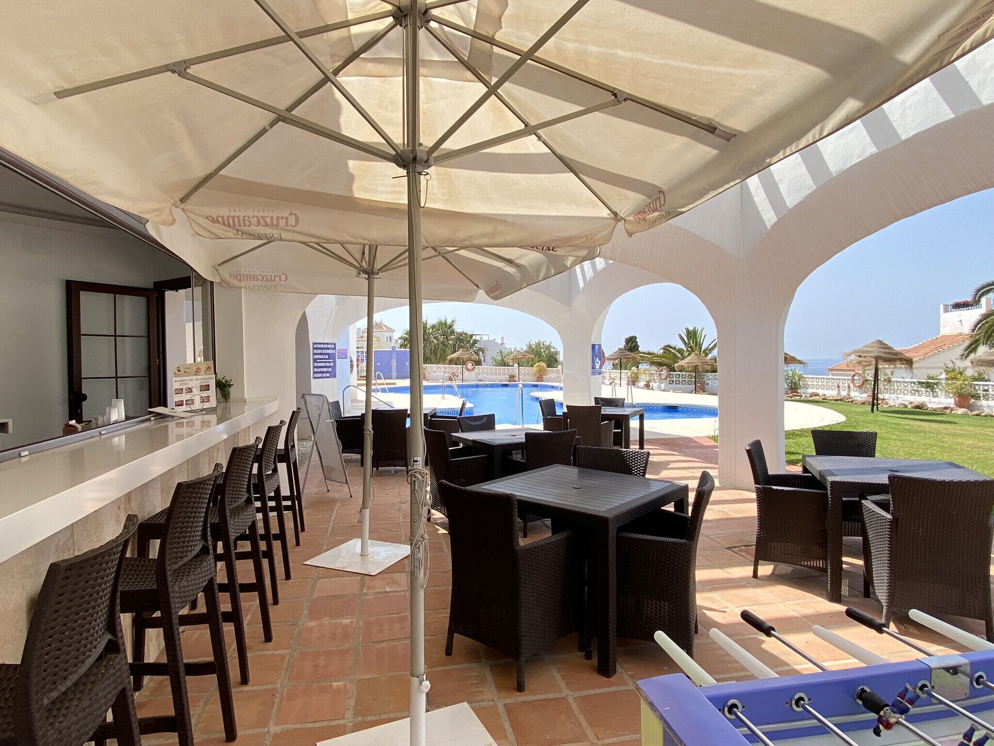 Ein Sitzbereich im Freien mit Tischen und Stühlen, im Hintergrund ein Pool und links eine Bar.