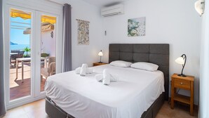 A hotel room with a bed, two nightstands, an air conditioner, a window with curtains, a table with chairs, and a view of the sea. - Capistrano Playa 404 by Casasol (Nerja)