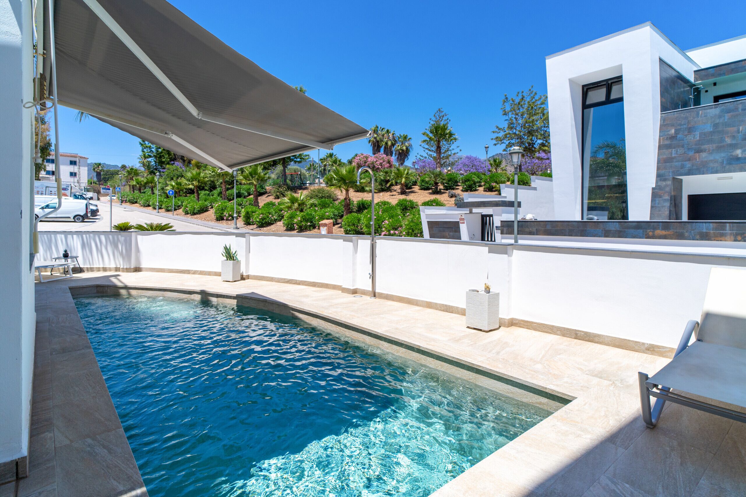Ein moderner Poolbereich mit klarem, blauem Pool, einer überdachten Sitzgelegenheit und einem angelegten Garten mit verschiedenen Pflanzen und Bäumen.