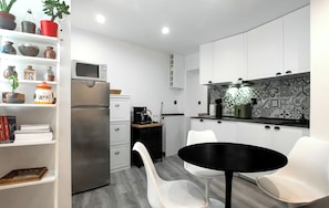 Une cuisine moderne avec des meubles blancs, un plan de travail noir et un coin repas blanc équipé de deux chaises.