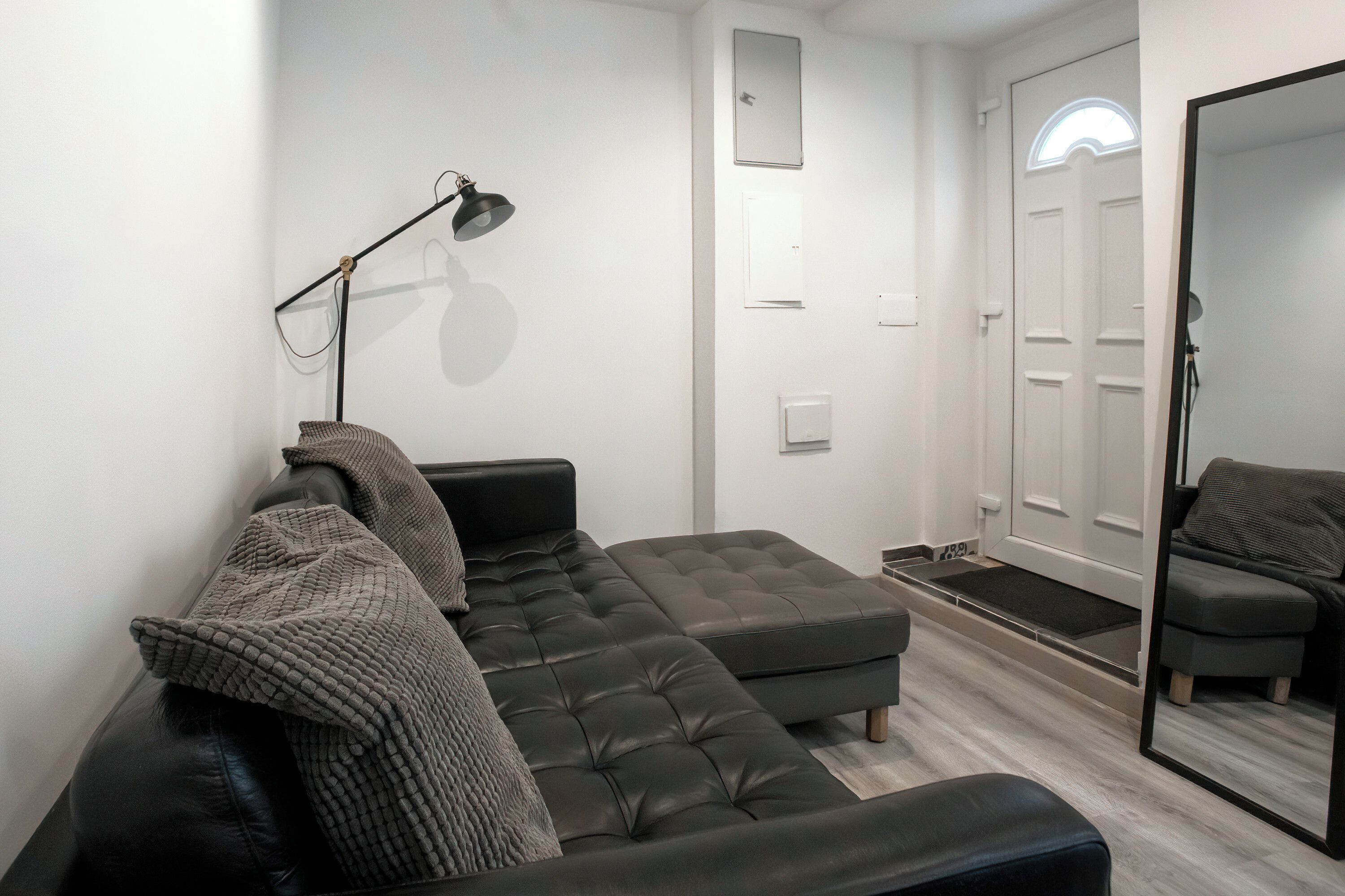 A modern living room with a sectional sofa, a standing lamp, and a large mirror.