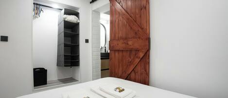A bedroom with a bed, two towels, a wooden sliding door, a white brick wall, and a black shelf unit.