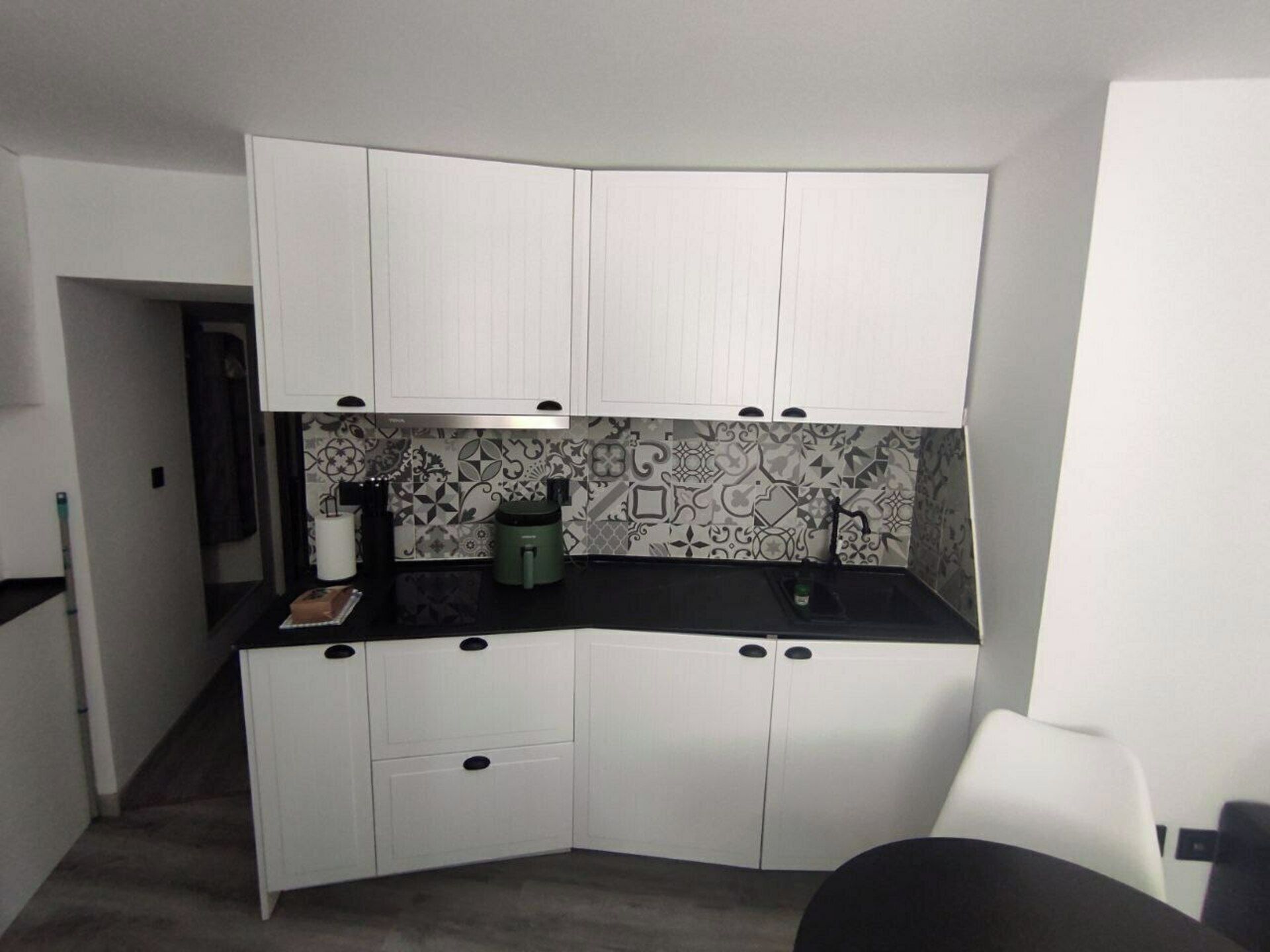 Cocina compacta con armarios blancos, encimera negra y azulejos decorativos en la pared.