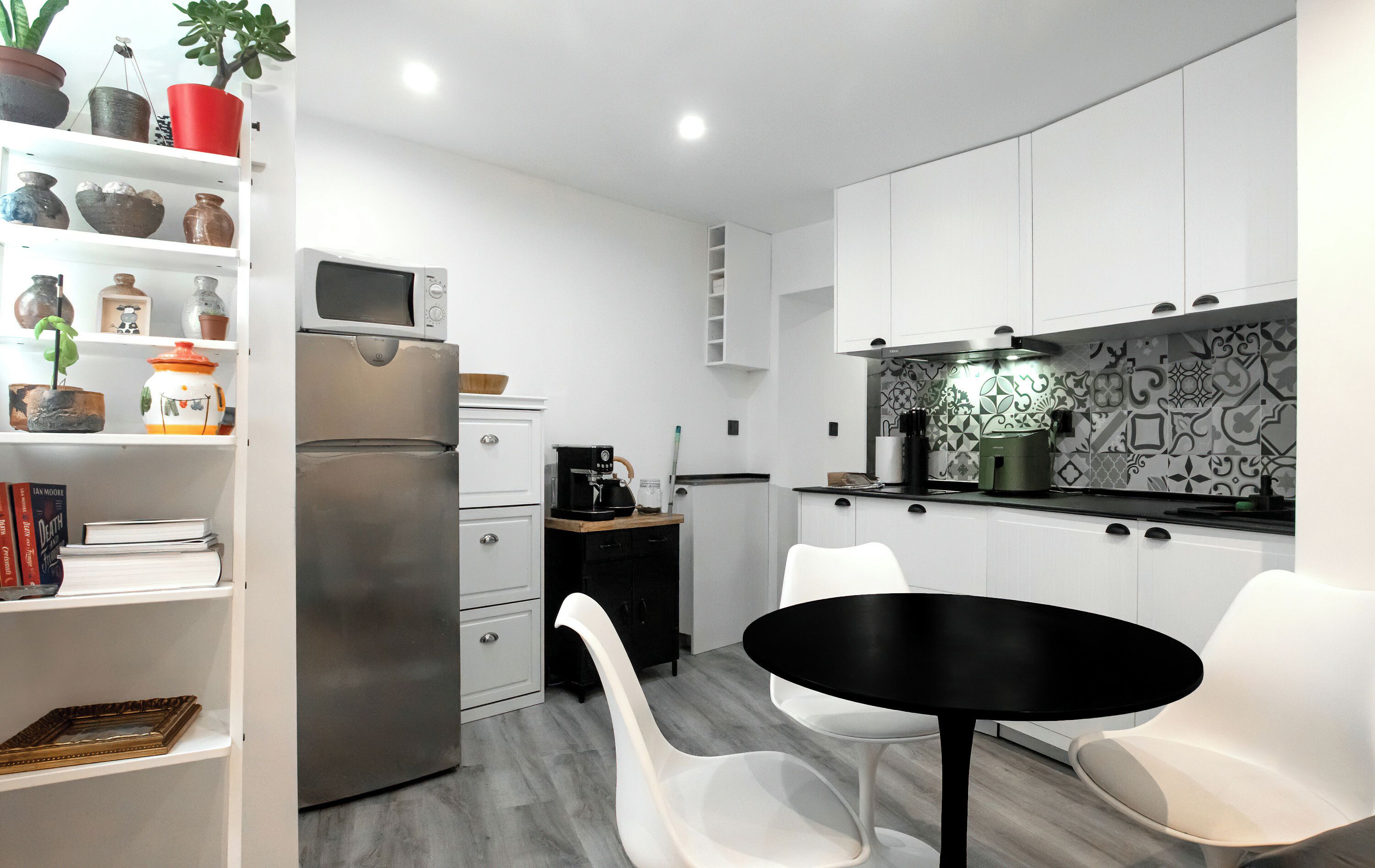A modern kitchen with white cabinetry, a black countertop, and a white dining area with two chairs.