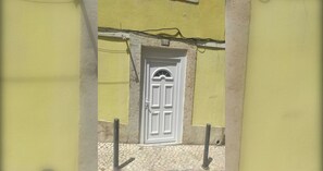 Une façade d’immeuble avec une porte blanche, un mur en pierre et un sol pavé.