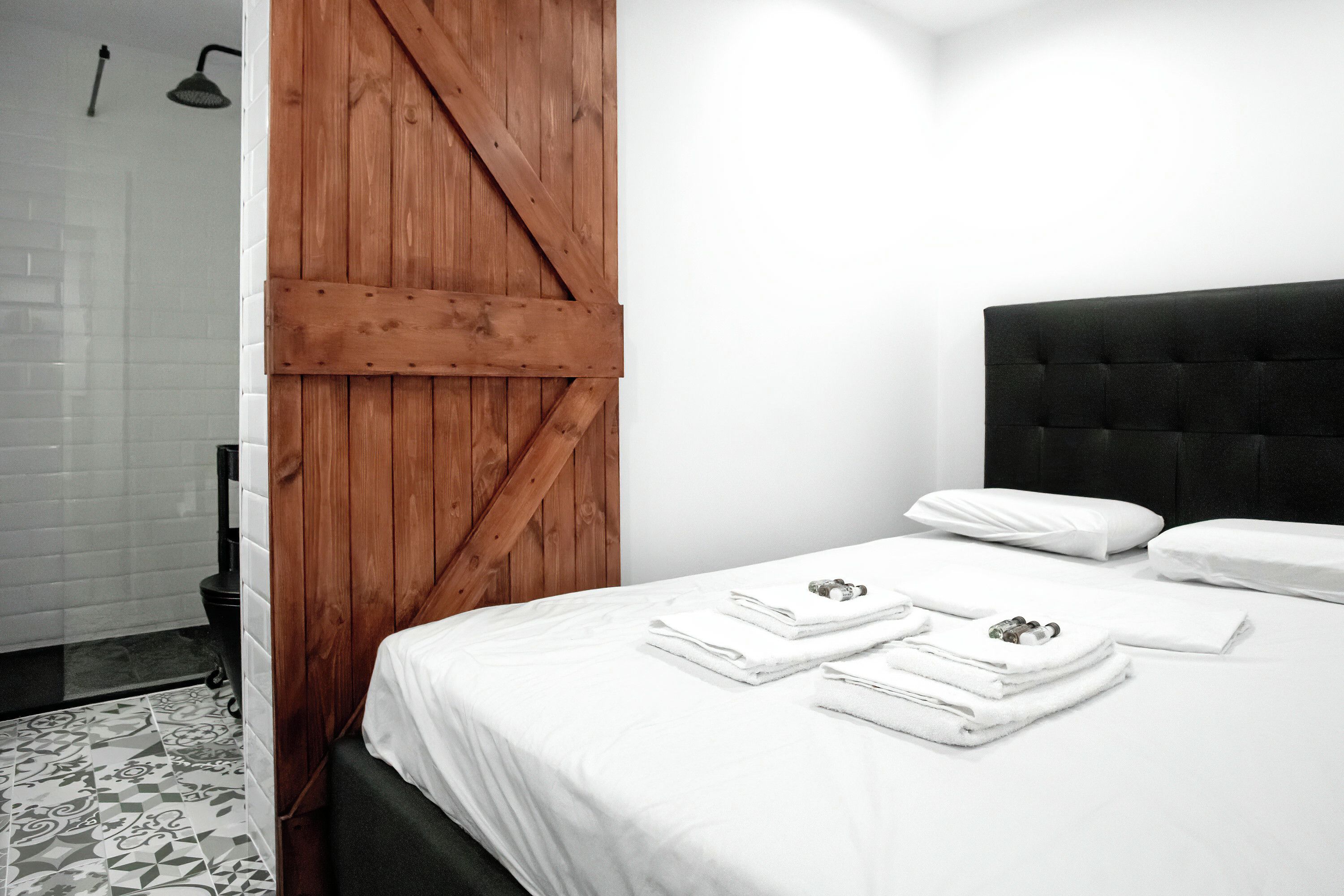 A hotel room with a bed, white linens, a wooden door, and a black headboard.
