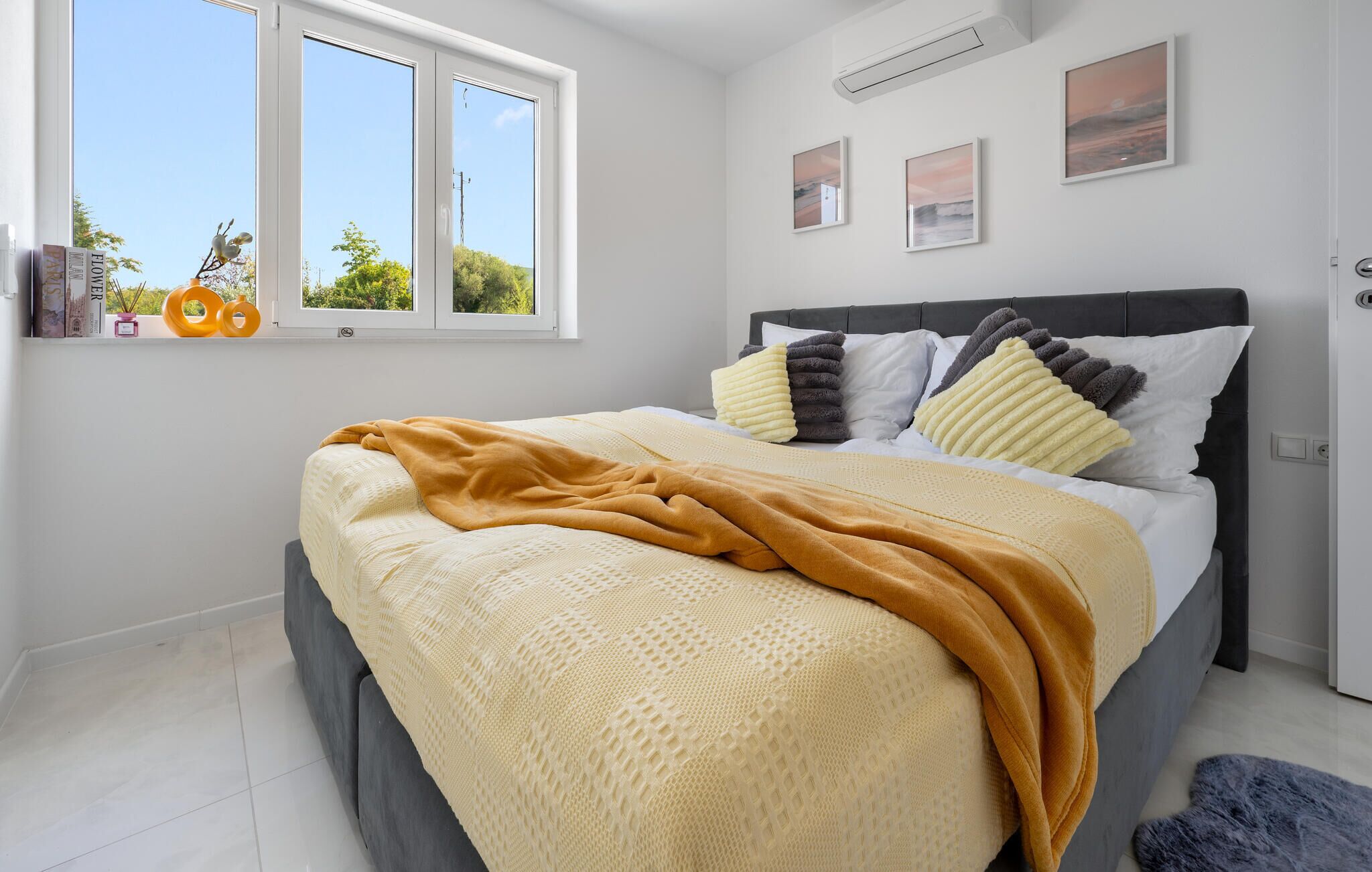 Un dormitorio con cama, almohadas, colcha, ventana y decoración en la pared.
