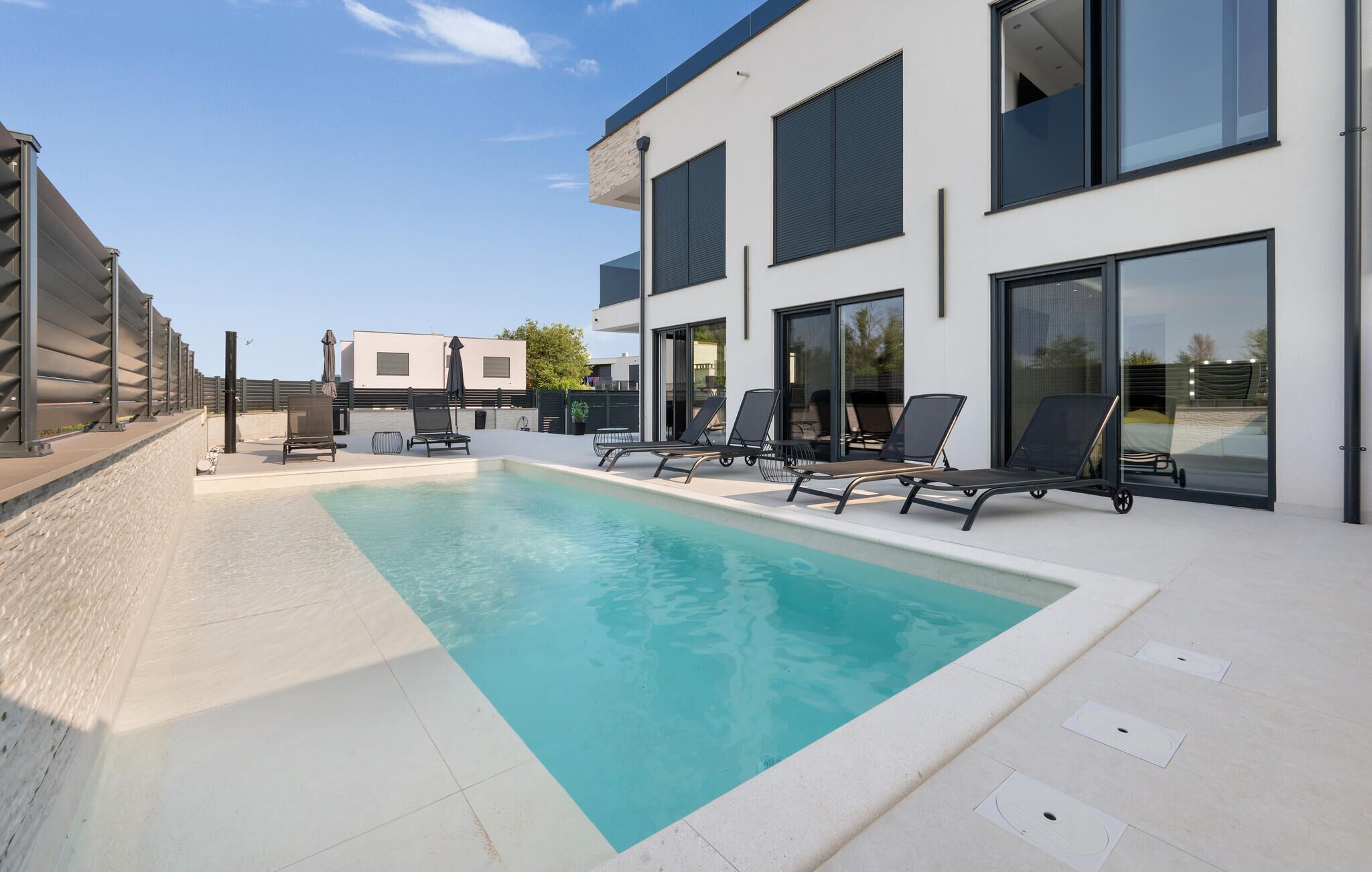 Un bâtiment moderne doté d’une piscine, de chaises longues et offrant une vue sur un ciel dégagé.