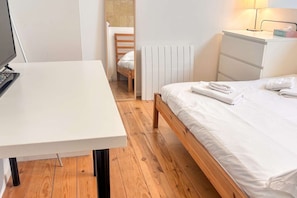 A bedroom with a wooden bed, white bedding, a white desk, and a radiator. - Apartment with a Mezzanine Bedroom Bordeaux (Bordeaux)