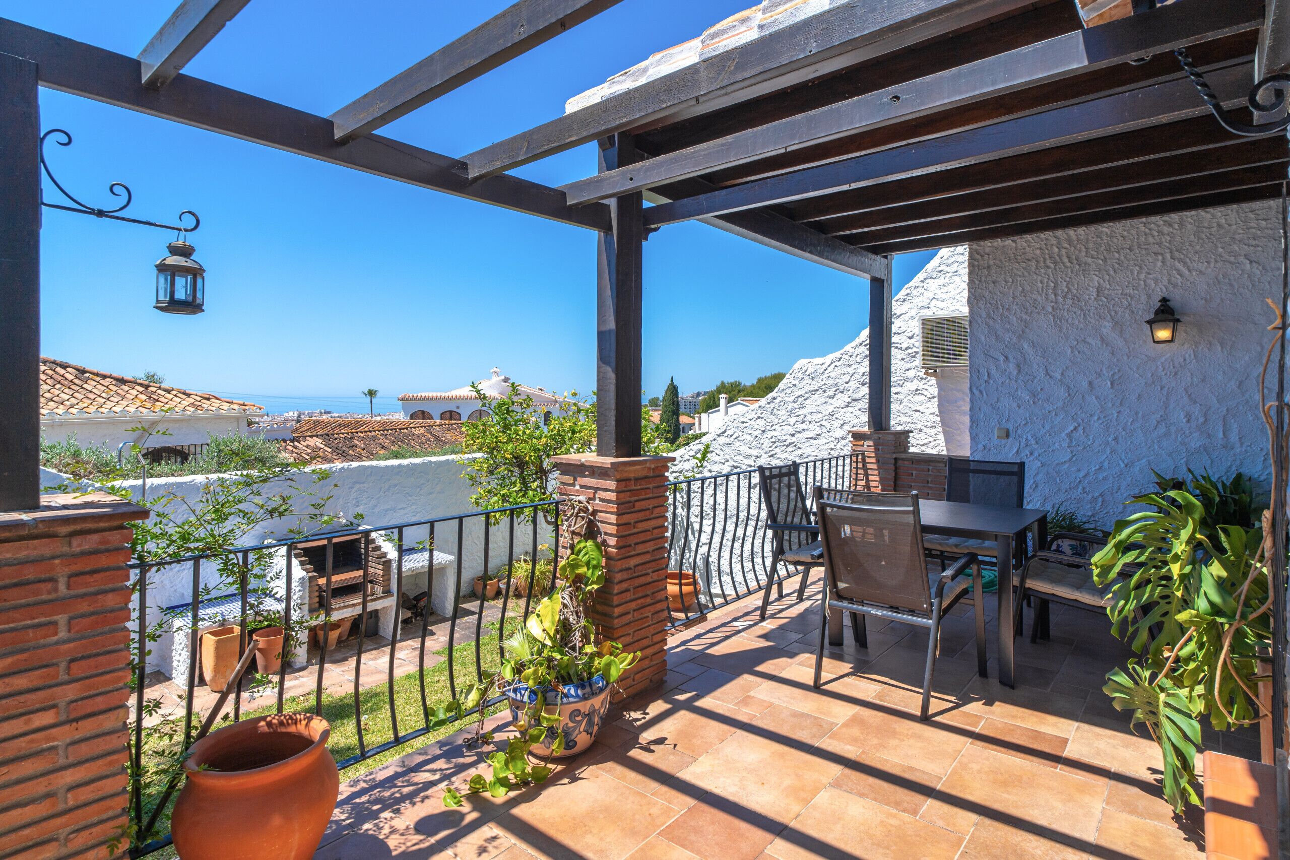 A patio with a table and chairs, potted plants, and a view of the sea.