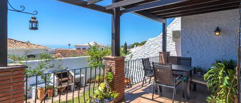 A patio with a table and chairs, potted plants, and a view of the sea.