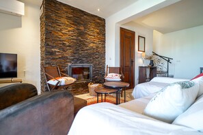 Ein gemütliches Wohnzimmer mit Steinwand, Kamin, Fernseher und bequemen Sitzgelegenheiten.