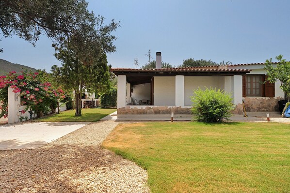 A house with a patio, a stone wall, and a garden with a tree and flowers.