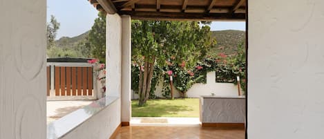 Eine überdachte Terrasse mit Fliesenboden, Holzboden und Blick auf einen Garten mit Bäumen und Blumen.