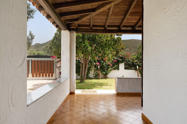 A covered patio with a tiled floor, a wooden ceiling, and a view of a garden with trees and flowers. - Villa Nino - Solanas, steps from the sea, private garden, up to 6 guests (Solanas)