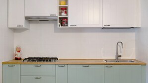 A kitchen with white cabinets, a gas stove, a sink, and a small shelf with kitchen utensils.
