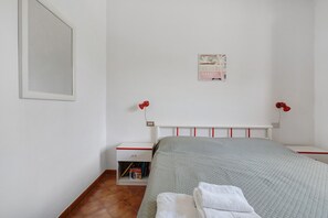 A bedroom with a bed, a nightstand, a wall-mounted lamp, and a poster on the wall.