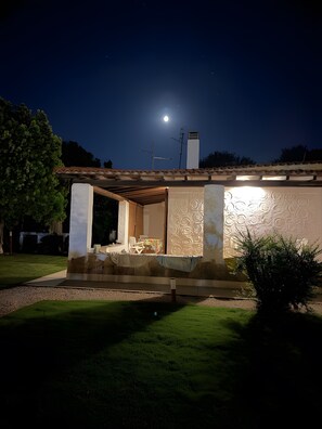 A house with a patio, a moon in the sky, and a tree.