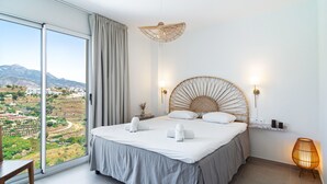 A bedroom with a large bed, a view of the countryside, a wicker headboard, and a bedside lamp. - Bayview Hills Deluxe by Casasol (Torrox)