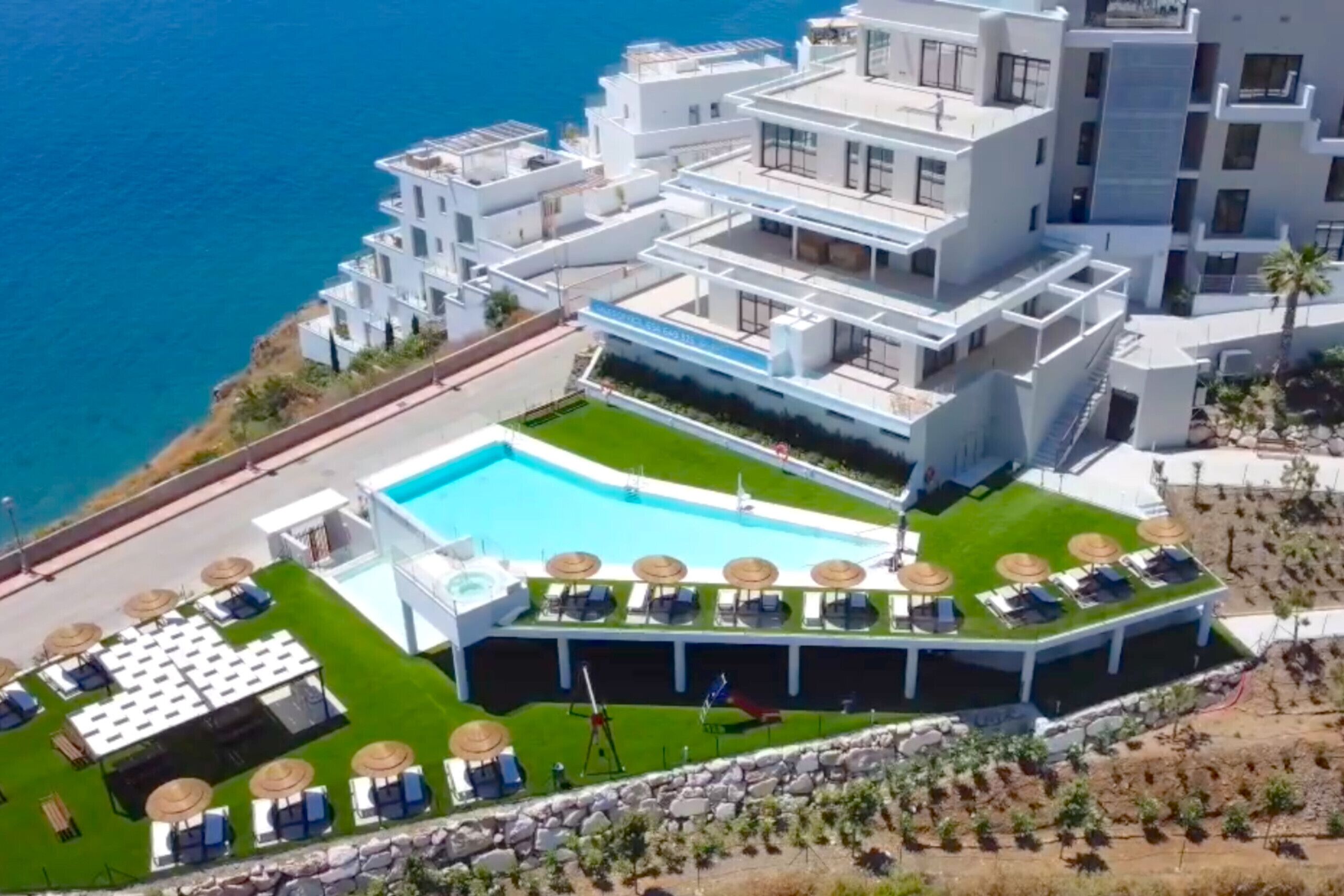 A modern hotel with a rooftop pool, multiple balconies, and a view of the sea.