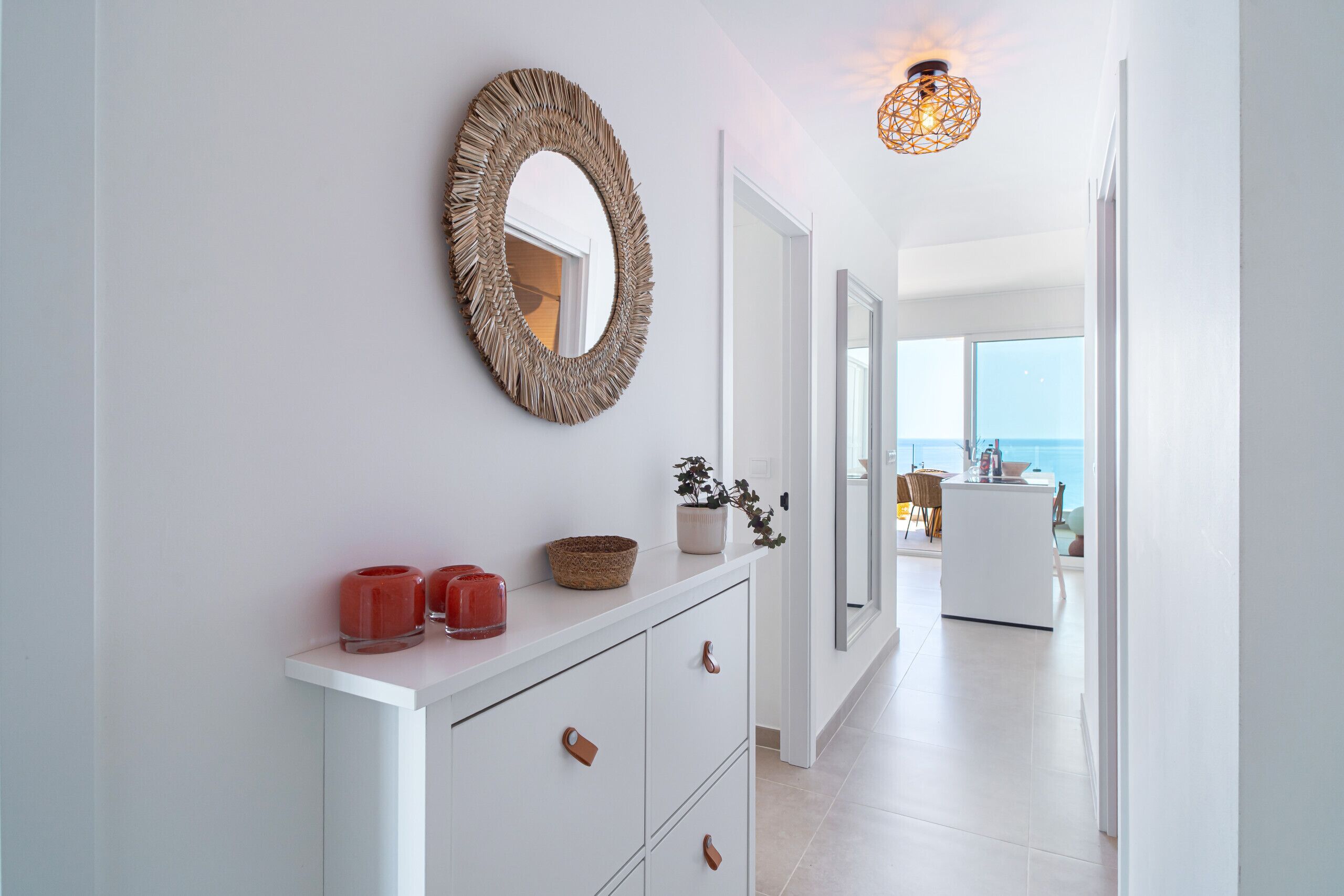 A modern hallway with a white console table, a woven mirror, and a hanging light fixture.