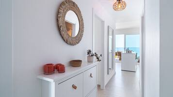 A modern hallway with a white console table, a woven mirror, and a hanging light fixture.