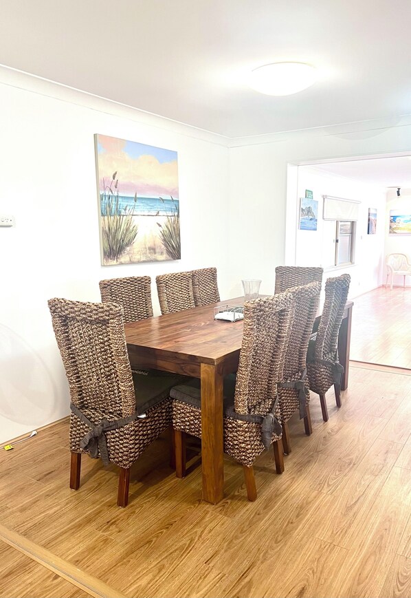 A dining area with a wooden table and patterned chairs, a painting on the wall, and a door in the background.
