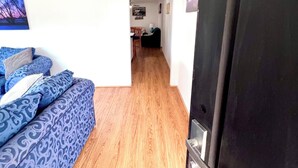 Une pièce avec un canapé bleu à motifs, un plancher en bois, une porte noire et un couloir menant à une autre pièce.