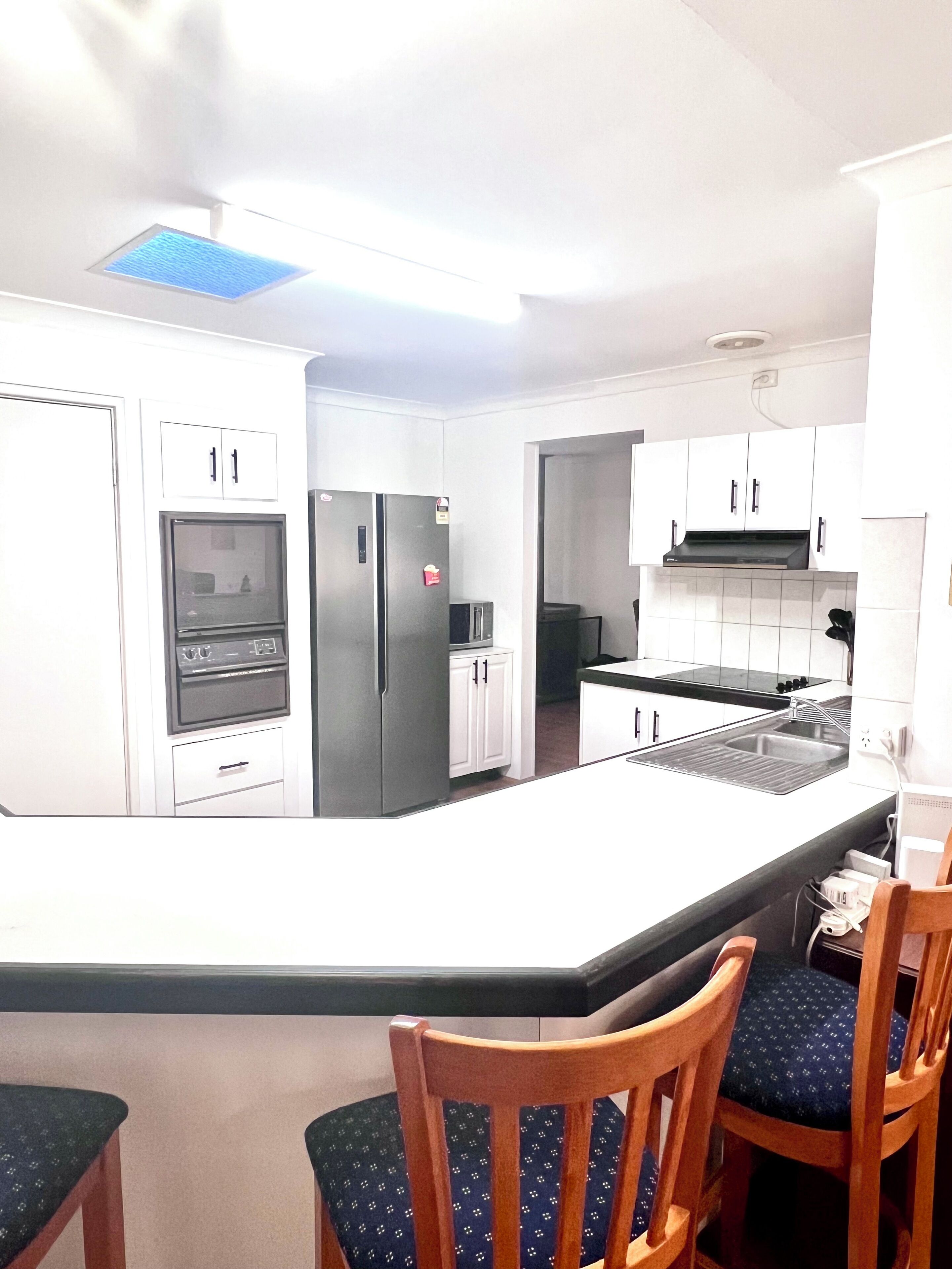 A modern kitchen with white cabinets, a built-in oven, a refrigerator, and a central island with chairs.