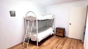 Une pièce avec un lit superposé, un plancher en bois, une petite armoire et une porte.