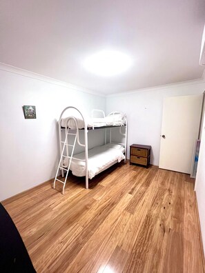 Une pièce avec un lit superposé, un plancher en bois, une petite armoire et une porte.