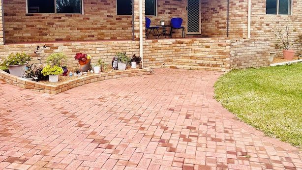 Un immeuble résidentiel à la façade en briques, doté d’un patio couvert avec des espaces pour s’asseoir à l’extérieur et d’un jardin bien entretenu.