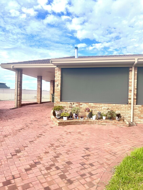 A covered outdoor area with a brick patio, a brick wall with a large window, and potted plants.