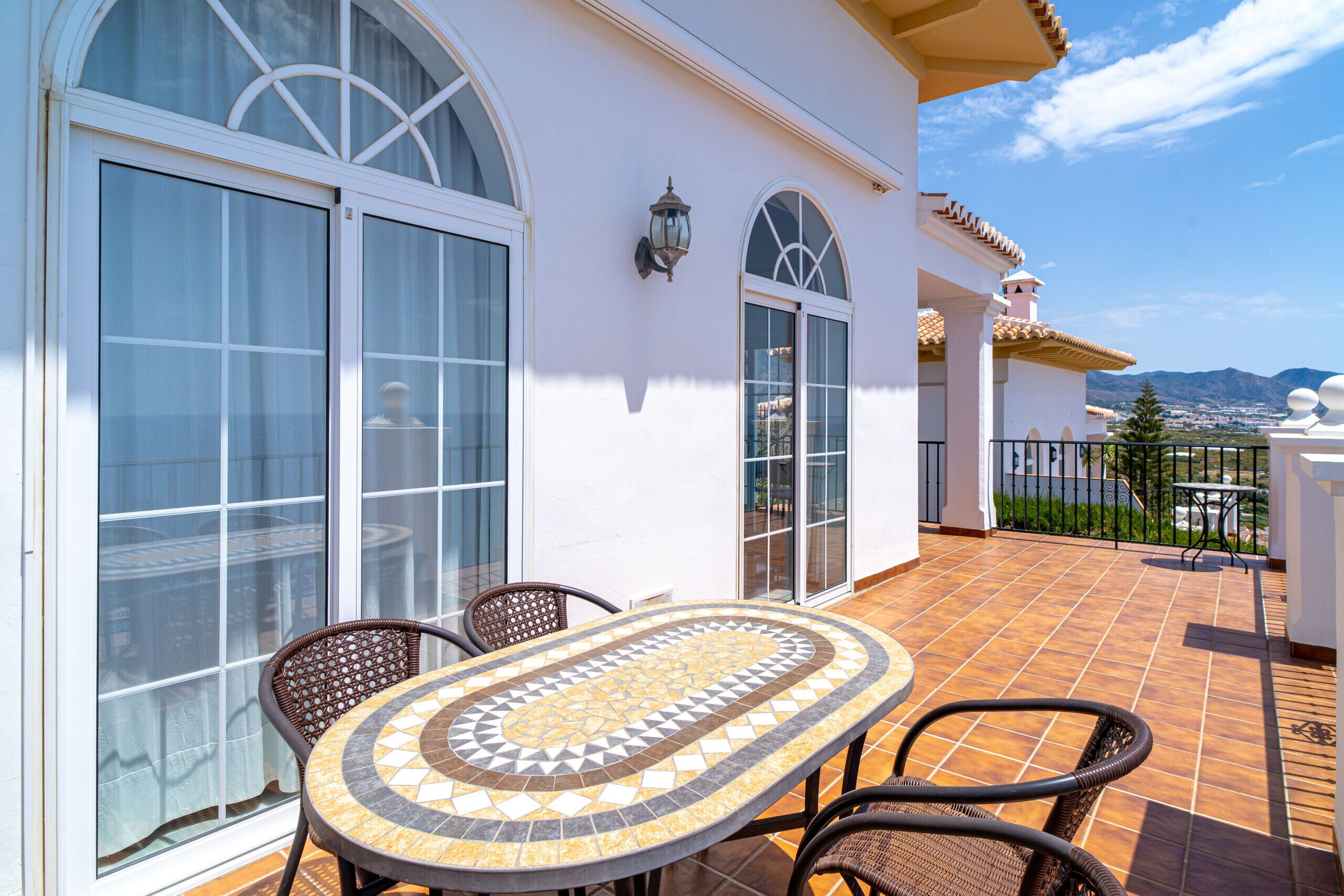 Une terrasse avec une table et des chaises carrelées, de grandes fenêtres et une vue sur le paysage.