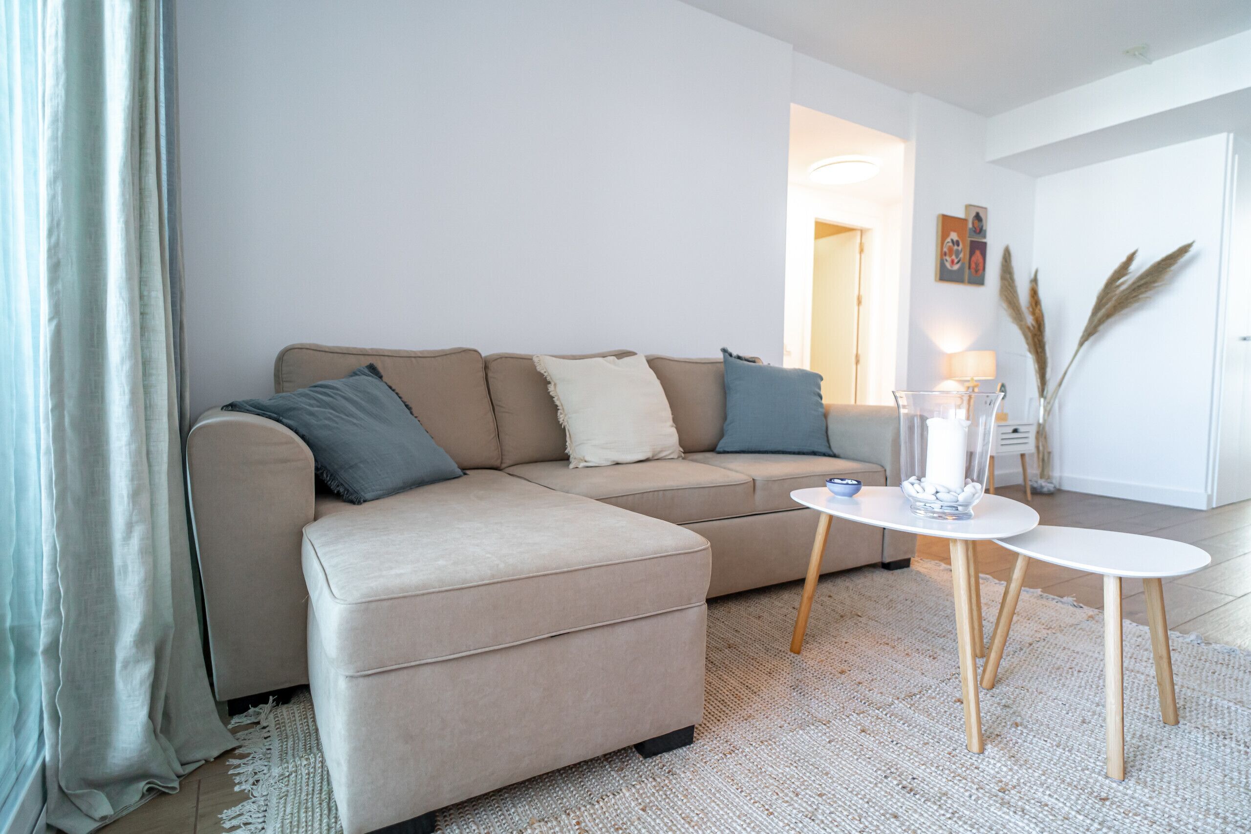 A living room with a beige sofa, two white side tables, and a small decorative vase.