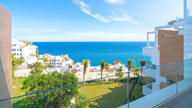 Un bâtiment moderne doté d’un balcon donnant sur une zone côtière, avec un ciel bleu dégagé et la mer.