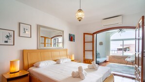 A well-lit bedroom with a large bed, bedside lamps, a ceiling fan, and a view through an open door to an outdoor area. - Casa Rosa Splash Pool by Casasol (Nerja)
