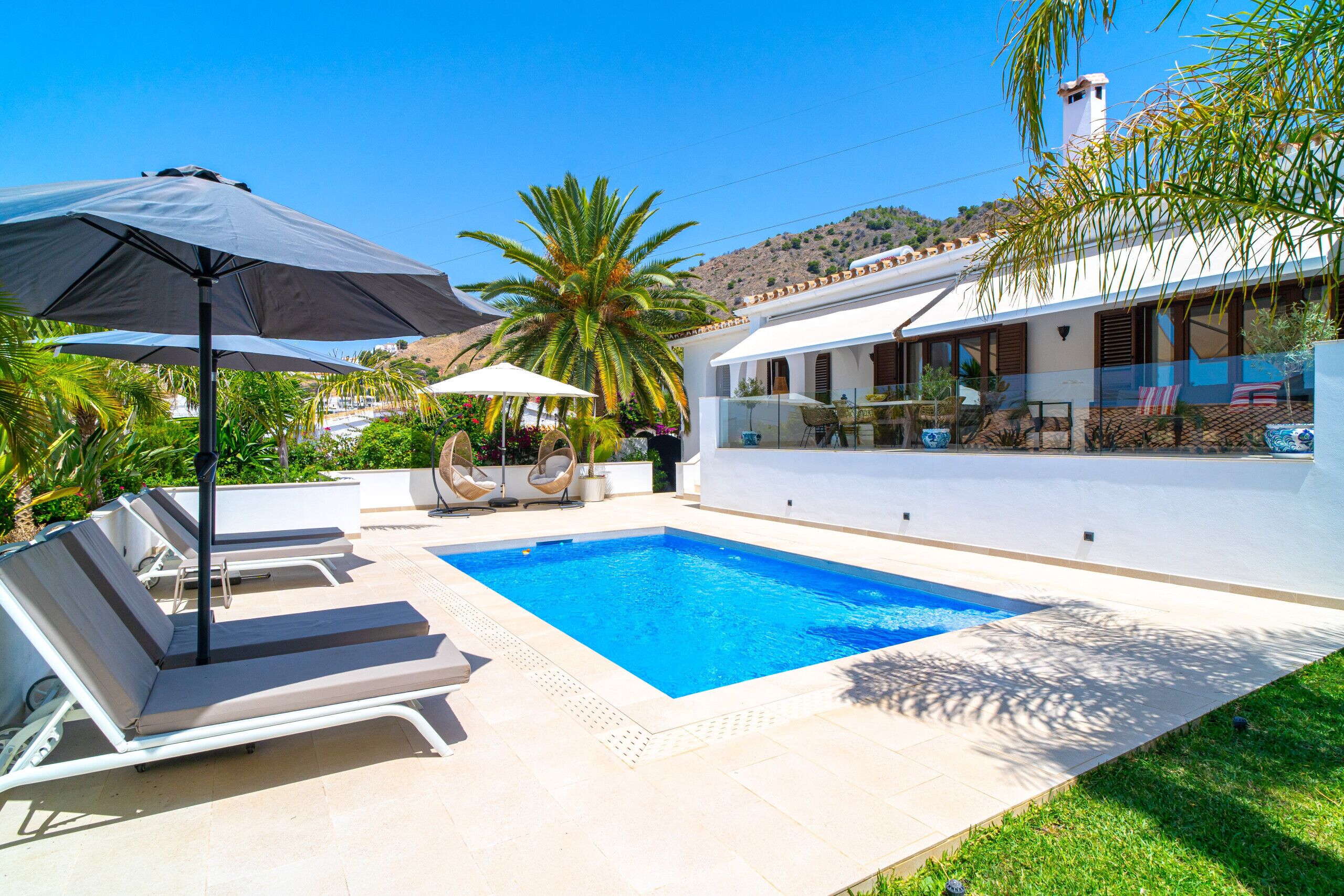 A swimming pool with lounge chairs and umbrellas, surrounded by greenery and a hillside view.