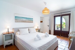 Ein ordentlich eingerichtetes Schlafzimmer mit Bett, Nachttischen, einer Hängelampe und Blick durch eine Tür.