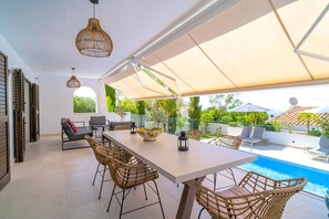 Eine sonnendurchflutete Terrasse mit Pool, Korbmöbeln und einem großen Tisch.