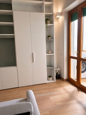 A room with a large white wardrobe, a wooden floor, and a sliding glass door leading to a laundry area. - Elegant apartment 2 km from Poetto (Quartu Sant'Elena)