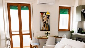 Un salon moderne avec un canapé blanc, une table à manger avec des chaises, un tableau au mur et un appareil de climatisation.
