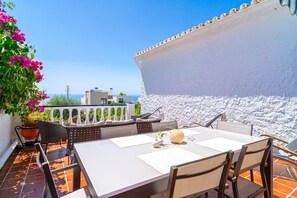 Una terrazza con tavolo e sedie bianche, una pianta in vaso e vista sul mare e sugli edifici.